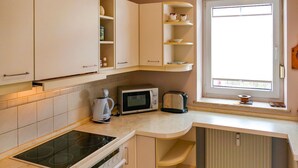 A kitchen with white cabinets, a built-in microwave, a coffee maker, and a window with blinds. - Vacation apartment Fraenzi - with wonderful sea view - Ferienappartement Fraenzi (Sassnitz auf Rügen)
