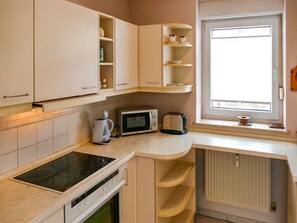 A kitchen with white cabinets, a built-in microwave, a coffee maker, and a window with blinds. - Vacation apartment Fraenzi - with wonderful sea view - Ferienappartement Fraenzi (Sassnitz auf Rügen)