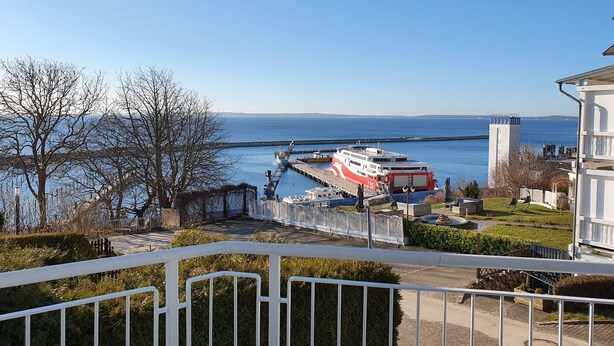 A waterfront view with a ferry docked, a white building with a balcony, and a clear sky. - Vacation apartment Fraenzi - with wonderful sea view - Ferienappartement Fraenzi (Sassnitz auf Rügen)