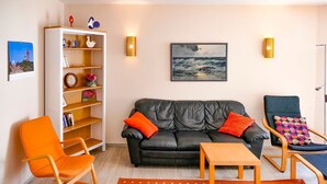 A living room with a black leather sofa, orange armchair, wooden coffee table, and a bookshelf with decorative items. - Vacation apartment Fraenzi - with wonderful sea view - Ferienappartement Fraenzi (Sassnitz auf Rügen)