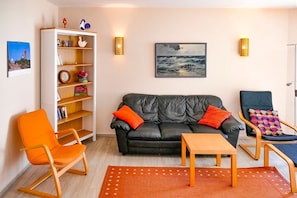 A living room with a black leather sofa, orange armchair, wooden coffee table, and a bookshelf with decorative items. - Vacation apartment Fraenzi - with wonderful sea view - Ferienappartement Fraenzi (Sassnitz auf Rügen)