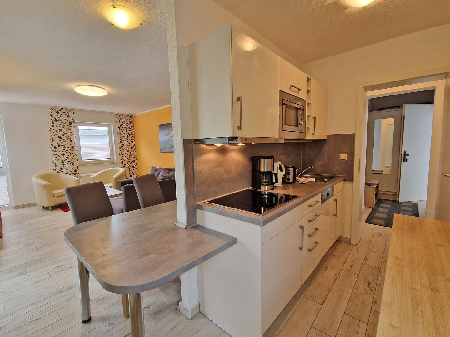 A modern kitchen with a dining area, wooden flooring, and a view of the living room.