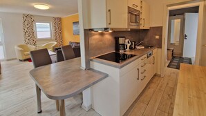 A modern kitchen with a dining area, wooden flooring, and a view of the living room. - Villa Monika, App. 5 Starboard - 2-room apartment with terrace and barbecue - (Sassnitz auf Rügen)