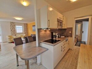 A modern kitchen with a dining area, wooden flooring, and a view of the living room. - Villa Monika, App. 5 Starboard - 2-room apartment with terrace and barbecue - (Sassnitz auf Rügen)