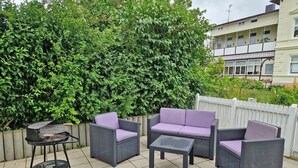 An outdoor patio with wicker furniture, a grill, and a white picket fence. - Villa Monika, App. 5 Starboard - 2-room apartment with terrace and barbecue - (Sassnitz auf Rügen)