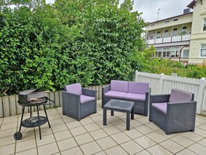 An outdoor patio with wicker furniture, a grill, and a white picket fence. - Villa Monika, App. 5 Starboard - 2-room apartment with terrace and barbecue - (Sassnitz auf Rügen)