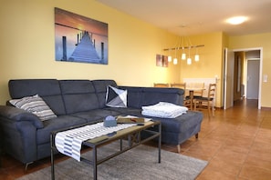 Ein Wohnzimmer mit einer Couch, einem Couchtisch, einem Gemälde und einem Essbereich mit Stühlen und Tisch.