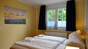 Ett hotellrum med två sängar, ett fönster med gardiner, ett element, en tavla på väggen och en liten skeppsdekoration på fönsterbrädan.