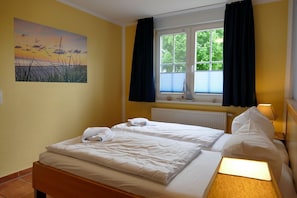 Ein Hotelzimmer mit zwei Betten, einem Fenster mit Vorhängen, einem Heizkörper, einem Bild an der Wand und einer kleinen Schiff-Dekoration am Fensterbrett.