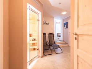 Ein Hotelzimmer mit Holztür, einer Glastür zum Sauna-Bereich und zwei Liegestühlen.