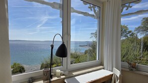 Una habitación con escritorio, silla y un ventanal con vistas a un cuerpo de agua.