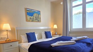 Habitación de hotel con cama, dos mesitas de noche, un cabecero, un cuadro en la pared y ventana con cortinas.
