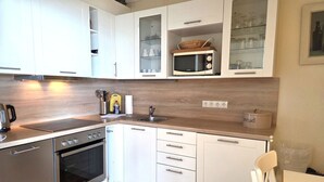 Una cocina moderna con armarios blancos, microondas, hervidor y un recipiente para pan.