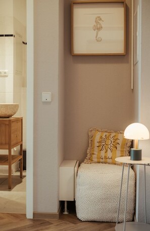 Ein Badezimmer mit Holzwaschtisch, einem gerahmten Kunstwerk mit einem Seepferdchen, einem flauschigen weißen Pouf und einem Tisch mit Lampe.