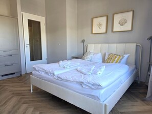 A neatly made bed with white linens and towels, a wardrobe, and two framed pictures on the wall. - Alter Reichshof, Apartment 303 with Ocean View and Balcony - Ocean View & Balcony in Alt (Sassnitz auf Rügen)