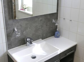 Ein Badezimmer mit einem weißen Waschbecken, einem Spiegel, einer Topfpflanze und einer Flasche Delrina Seife.