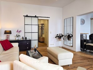 A modern living room with a sofa, ottoman, coffee table, and a sliding door leading to a bathroom. - Villa Seestern, apartment 1 - pure sea view! - Villa Seestern, vacation apartment 1 - (Sassnitz)