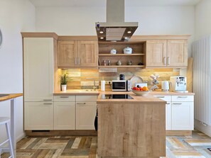 A modern kitchen with wooden cabinets, a central island, a microwave, a coffee machine, and a potted plant. - Villa Seestern, apartment 1 - pure sea view! - Villa Seestern, vacation apartment 1 - (Sassnitz)