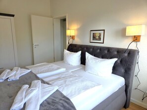 A hotel room with a large bed, two bedside lamps, a framed picture on the wall, and a door to another room. - Alter Reichshof, App. 307 - Alter Reichshof, App. 307 - with balcony (Sassnitz auf Rügen)