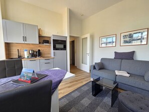 A modern living room with a grey sofa, a coffee table, and a dining area with a kitchen in the background. - Alter Reichshof, App. 307 - Alter Reichshof, App. 307 - with balcony (Sassnitz auf Rügen)