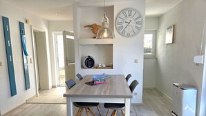 A modern dining area with a wooden table, chairs, a clock, and a small kitchen area with a refrigerator. - Seemeile 1 - Villa Monika - Villa Monika, App. Seemeile 1 with terrace (Sassnitz auf Rügen)