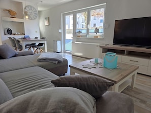 Ein modernes Wohnzimmer mit einer Couch, einem Couchtisch, einem Fernseher und einem Fenster mit Blick auf Gebäude.