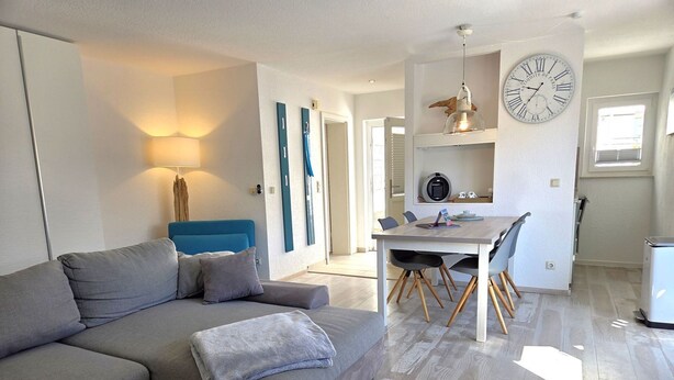 A modern living room with a grey sofa, a wooden coffee table, and a dining area with a white table and chairs. - Seemeile 1 - Villa Monika - Villa Monika, App. Seemeile 1 with terrace (Sassnitz auf Rügen)