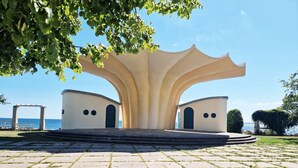 A symmetrical architectural structure with a central archway and two smaller arches on either side, set on a paved area with grass patches. - Fürstenhof, App.104 - First row by the sea - Fürstenhof, App. 104 - First row (Sassnitz auf Rügen)