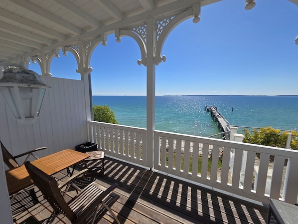 A covered outdoor area with a wooden table and chairs, a white railing, and a view of the ocean and a pier. - Fürstenhof, App.104 - First row by the sea - Fürstenhof, App. 104 - First row (Sassnitz auf Rügen)