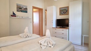 A hotel room with two beds, a television, a wardrobe, and a shelf with a boat model. - Fürstenhof, App.104 - First row by the sea - Fürstenhof, App. 104 - First row (Sassnitz auf Rügen)