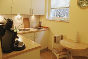 Eine kleine Küche mit Spüle, Schneidebrett, Toaster und einem kleinen Esstisch mit einem Stuhl.