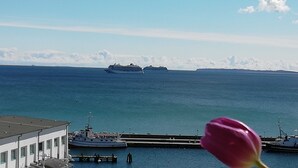 A large cruise ship in the distance, a docked boat, and a building with a view of the water. - Apartment Kapitänsmesse - fantastic view over the harbor and the sea - (Sassnitz auf Rügen)