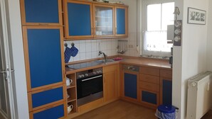 A compact kitchen with wooden cabinets, a built-in oven, a sink, and a window. - Apartment Kapitänsmesse - fantastic view over the harbor and the sea - (Sassnitz auf Rügen)