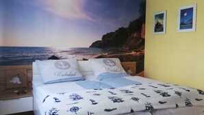 A bedroom with a bed, a nightstand, a lamp, and a wall with a nautical-themed mural. - Apartment Kapitänsmesse - fantastic view over the harbor and the sea - (Sassnitz auf Rügen)