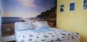 Ein Schlafzimmer mit Bett, Nachttisch, Lampe und einer Wand mit einem maritimen Wandgemälde.
