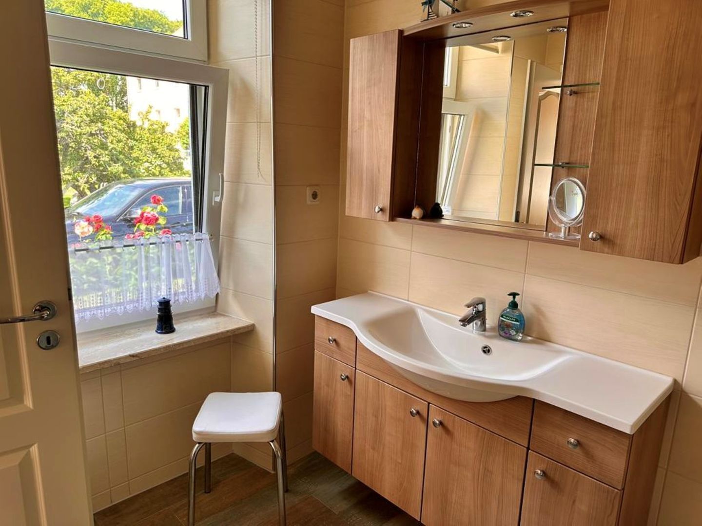 A bathroom with a window, a sink, a mirror, and wooden cabinets.
