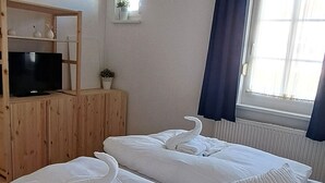 Hotellihuone, jossa on kaksi sänkyä, televisio puukehikossa, pieni huonekasvi ja ikkuna, jossa on verhot.