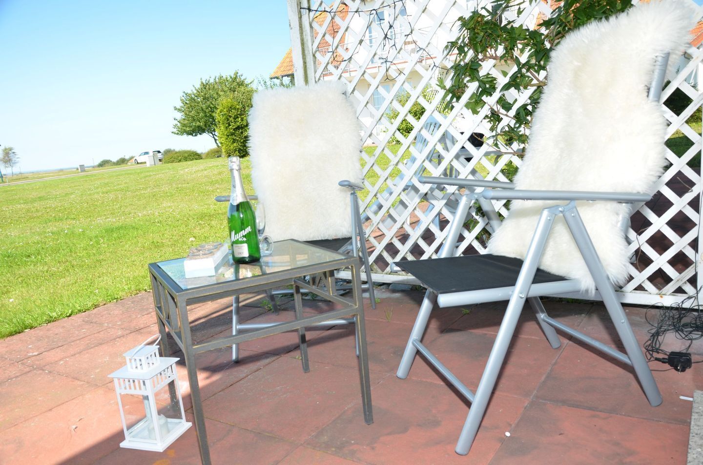 Un patio con mesa de vidrio, una botella de champán y una silla blanca.