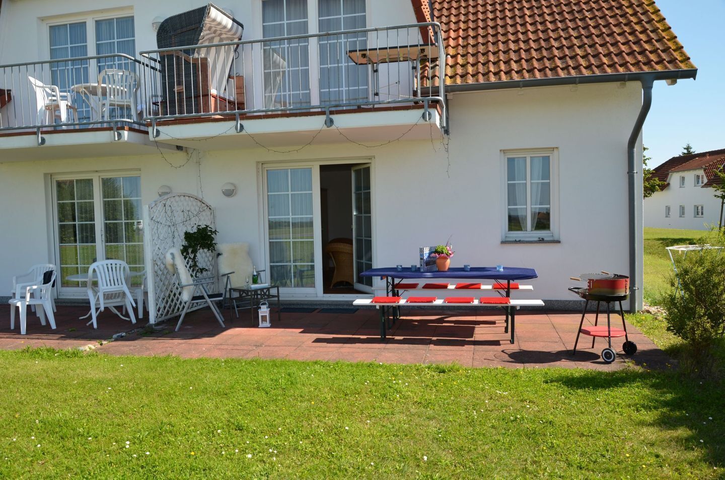 Ein zweistöckiges Haus mit Balkon, einer Terrasse mit Tisch und Stühlen sowie einem Grill.