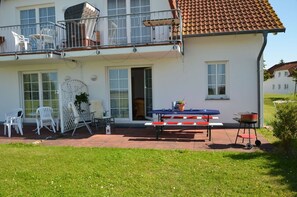 Ein zweistöckiges Haus mit Balkon, einer Terrasse mit Tisch und Stühlen sowie einem Grill.