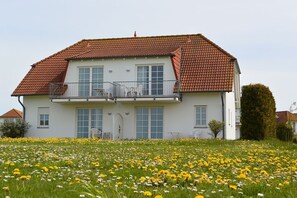 Ein zweistöckiges Haus mit rotem Ziegeldach, einem Balkon mit Gartenmöbeln und einem Garten mit gelben Blumen.