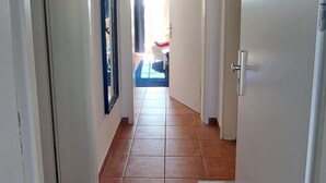 Käytävä, jossa on laatoitettu lattia, hopeanvärinen vetimellä varustettu ovi ja peili vasemmalla seinällä.