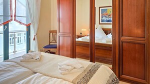 Una habitación de hotel con una cama, un armario de madera, una ventana con cortinas y un cuadro en la pared.