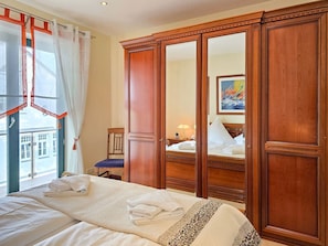 Ein Hotelzimmer mit Bett, Holzschrank, einem Fenster mit Vorhängen und einem Bild an der Wand.