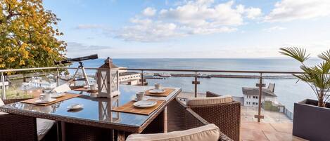 A terrace with wicker furniture, a telescope, and a view of the sea.