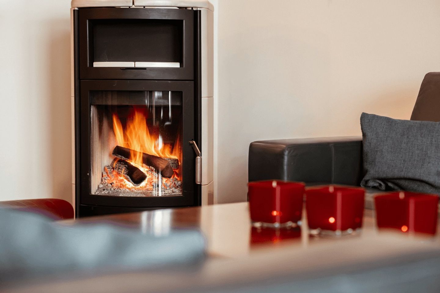 A modern fireplace with a glass front, logs burning, and a cozy seating area with a cushion and candles.