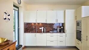 Una cocina moderna con gabinetes blancos, encimera de granito, pileta de acero inoxidable y horno integrado.