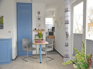 A room with a blue door, a small table with two chairs, a vase with flowers, and a window with blinds. - Apartment with Ocean View and 2 Balconies, Villa Monika, Apt. 7 - Villa Monika, Apt. 7 (Sassnitz auf Rügen)