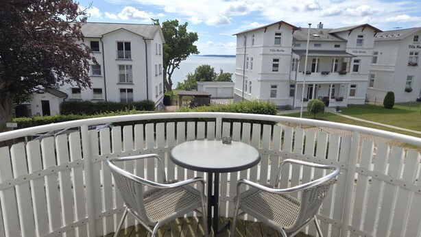 A balcony with a round table and two chairs, overlooking a body of water and a row of white buildings with balconies. - Apartment with Ocean View and 2 Balconies, Villa Monika, Apt. 7 - Villa Monika, Apt. 7 (Sassnitz auf Rügen)