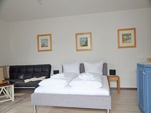A bedroom with a bed, a black leather sofa, a small table, and framed pictures on the wall. - Apartment with Ocean View and 2 Balconies, Villa Monika, Apt. 7 - Villa Monika, Apt. 7 (Sassnitz auf Rügen)